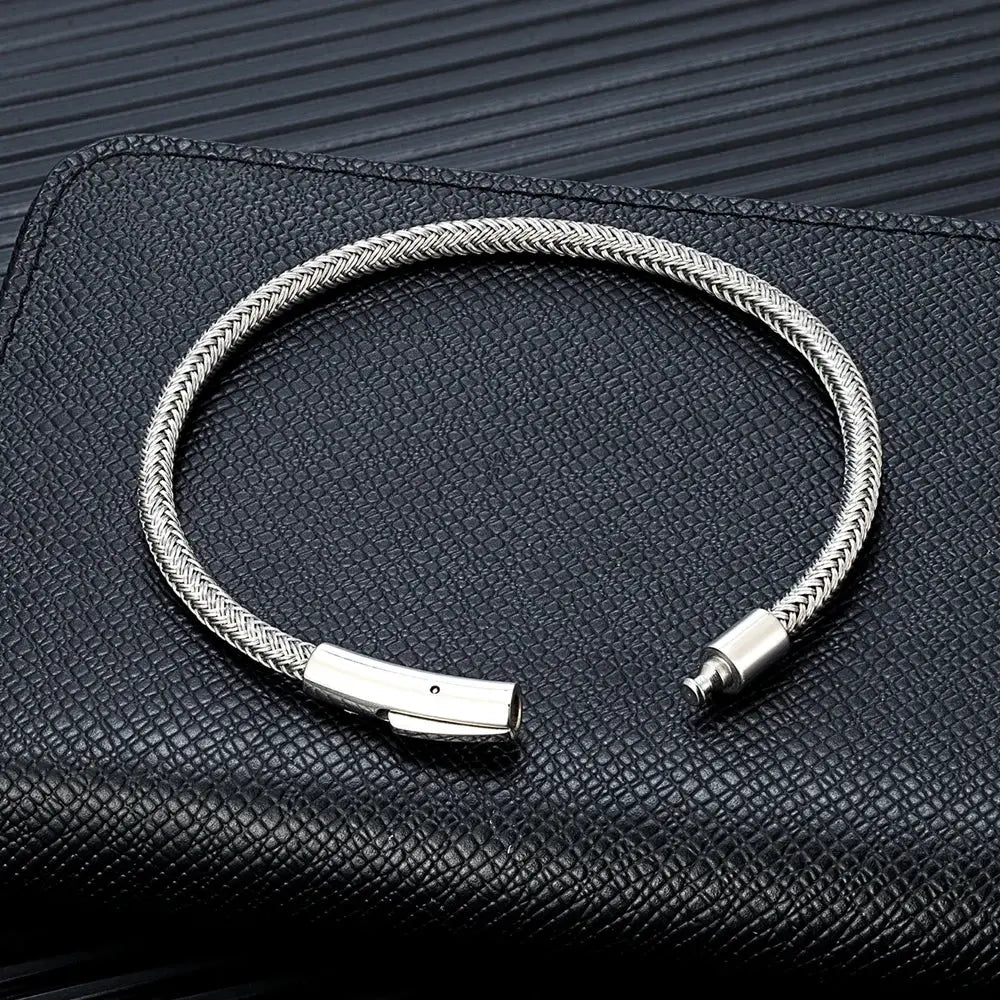 silver wire rope bracelet for man buckle bracelet with secure clasp, laid flat on black textured background for detailed view.